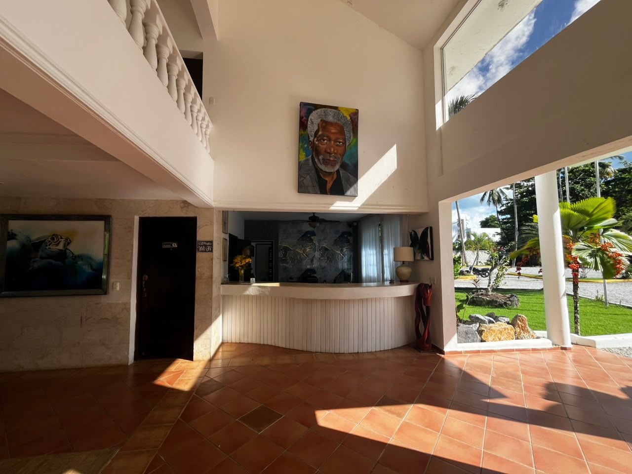 A spacious lobby with a reception desk, a painting above it, and a view of the outdoors.
