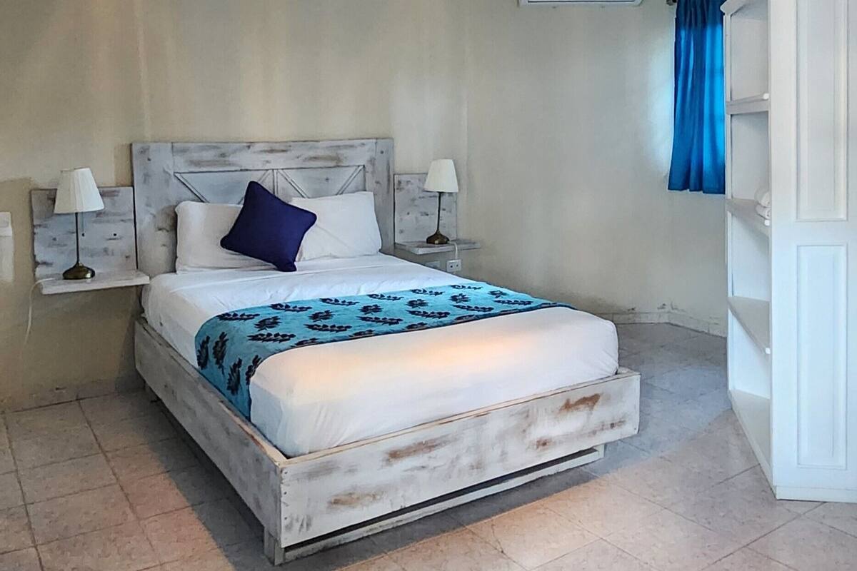 A bedroom with a bed, two bedside lamps, a ceiling light, an air conditioning unit, and a wardrobe.