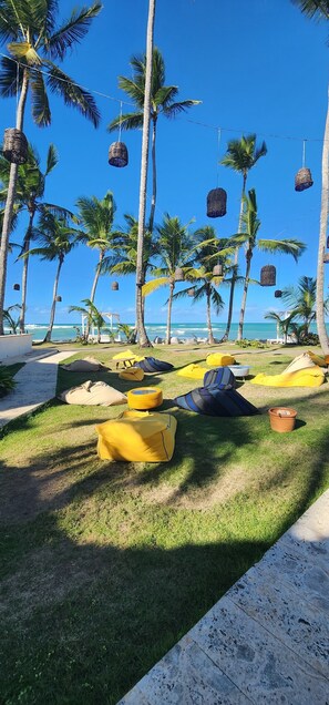 A beach setting with palm trees, hanging baskets, and beach chairs. - Hotel Bahia Punta Bonita (Las Terrenas)