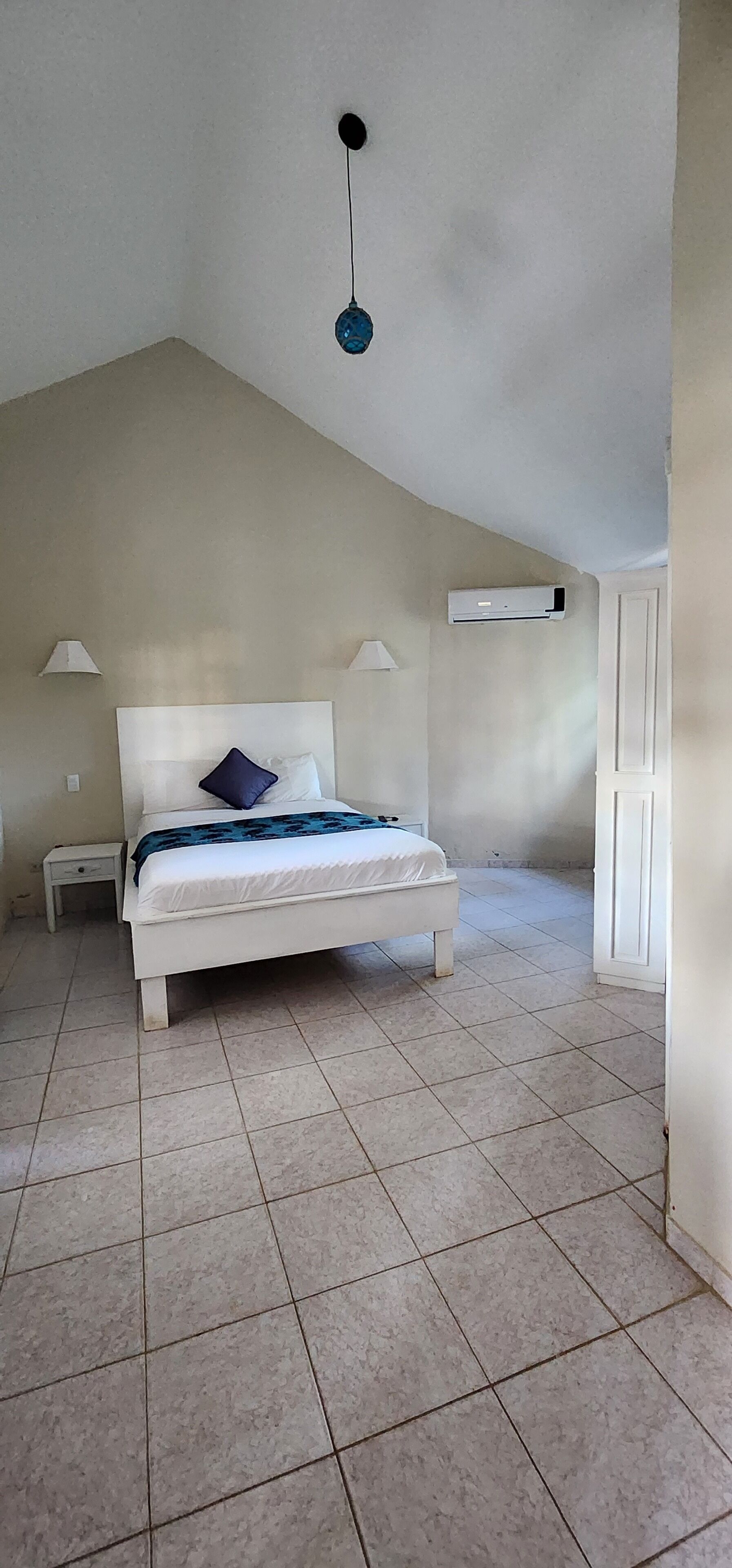 A bedroom with a bed, nightstands, a ceiling light, and an air conditioning unit.