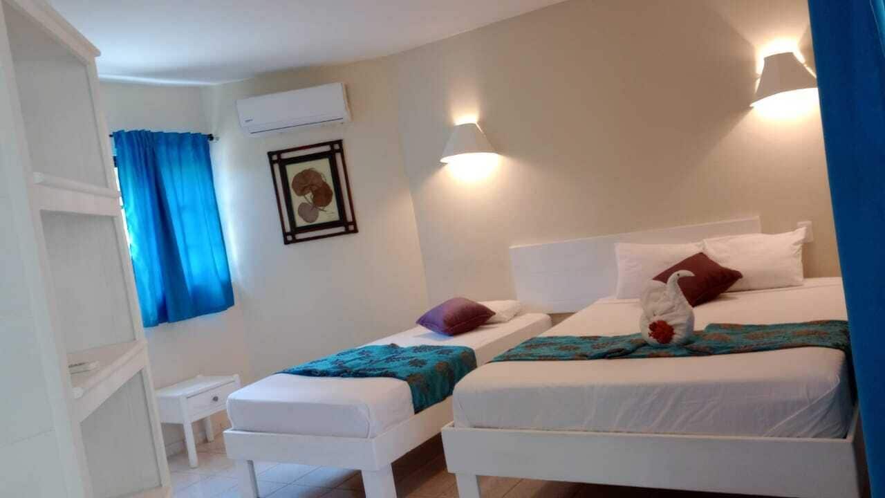 A room with two single beds, a small bedside table, a wall-mounted air conditioner, and a framed picture.