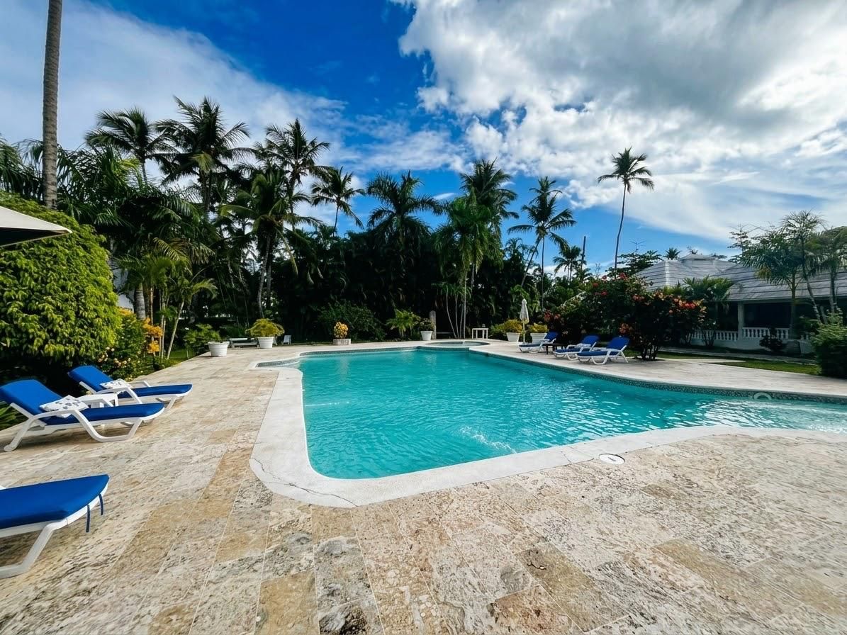 A swimming pool with lounge chairs, surrounded by palm trees and a clear sky.