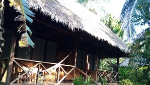 Eine Holzhütte mit einem Strohdach und einer Holzdar Terrasse. Ein Feuerlöscher ist an der Wand angebracht.