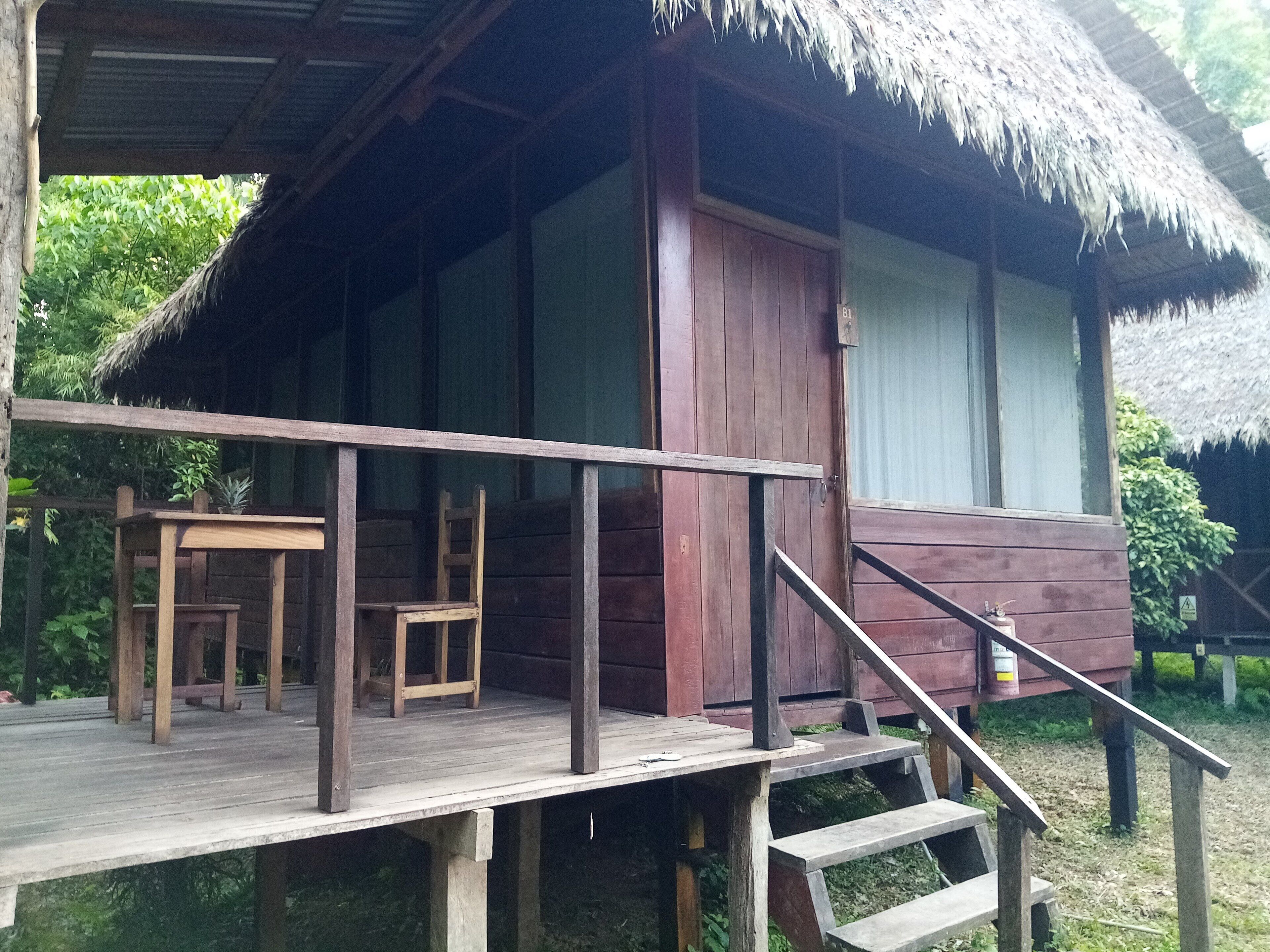 A wooden cabin with a thatched roof, a wooden deck, and a staircase leading to the entrance.