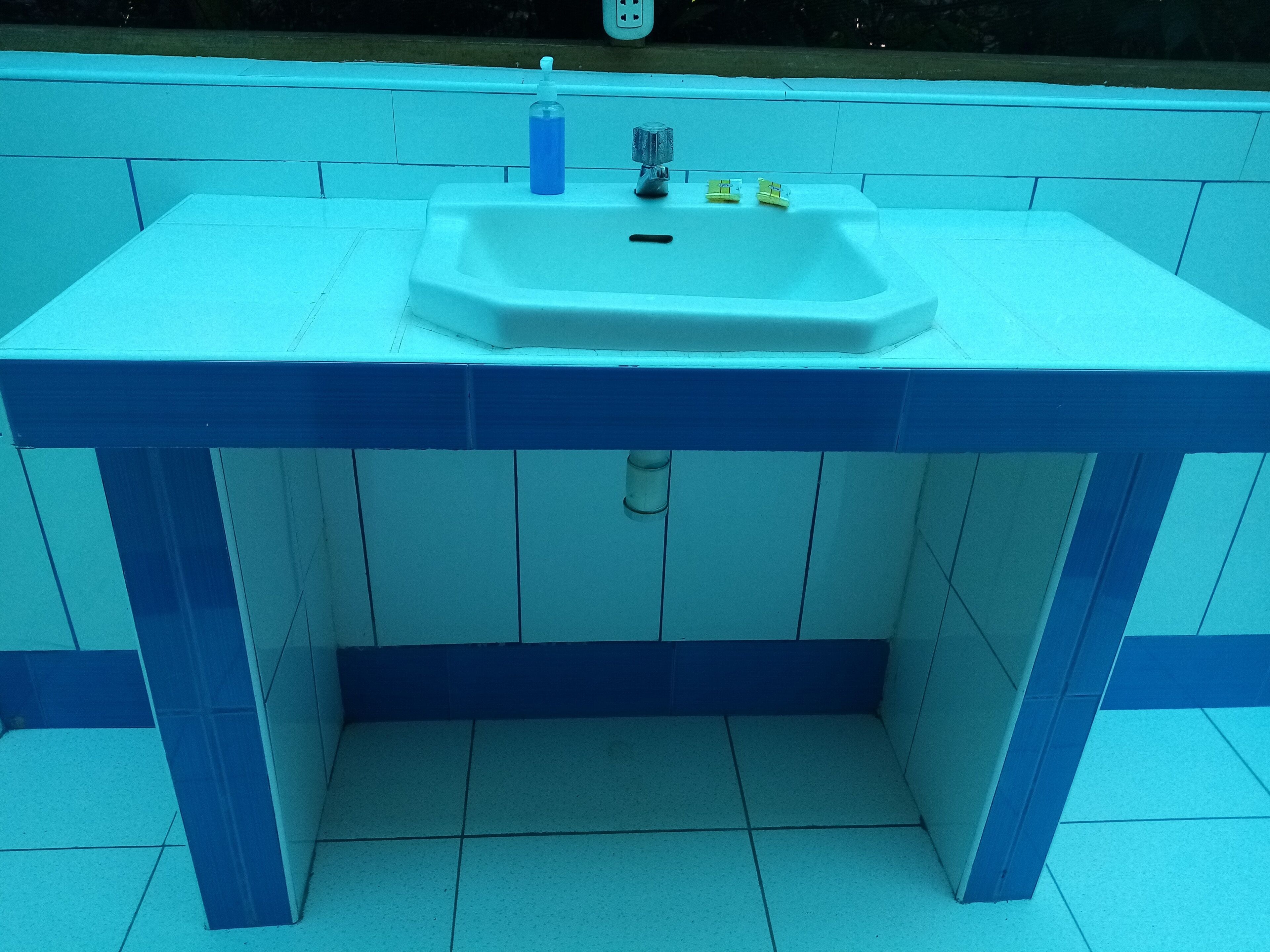 Un baño con un lavamanos blanco, paredes con azulejos azules y suelo blanco.