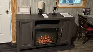 Un salon doté d’un téléviseur à écran plat fixé au-dessus d’un meuble de rangement en bois foncé, d’une cheminée et d’une fenêtre ornée de rideaux en dentelle.