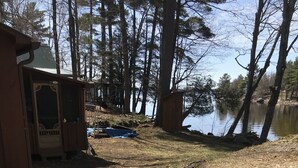 Un terrain de camping avec un chalet en bois, une tente et un petit bateau au bord d’un lac.