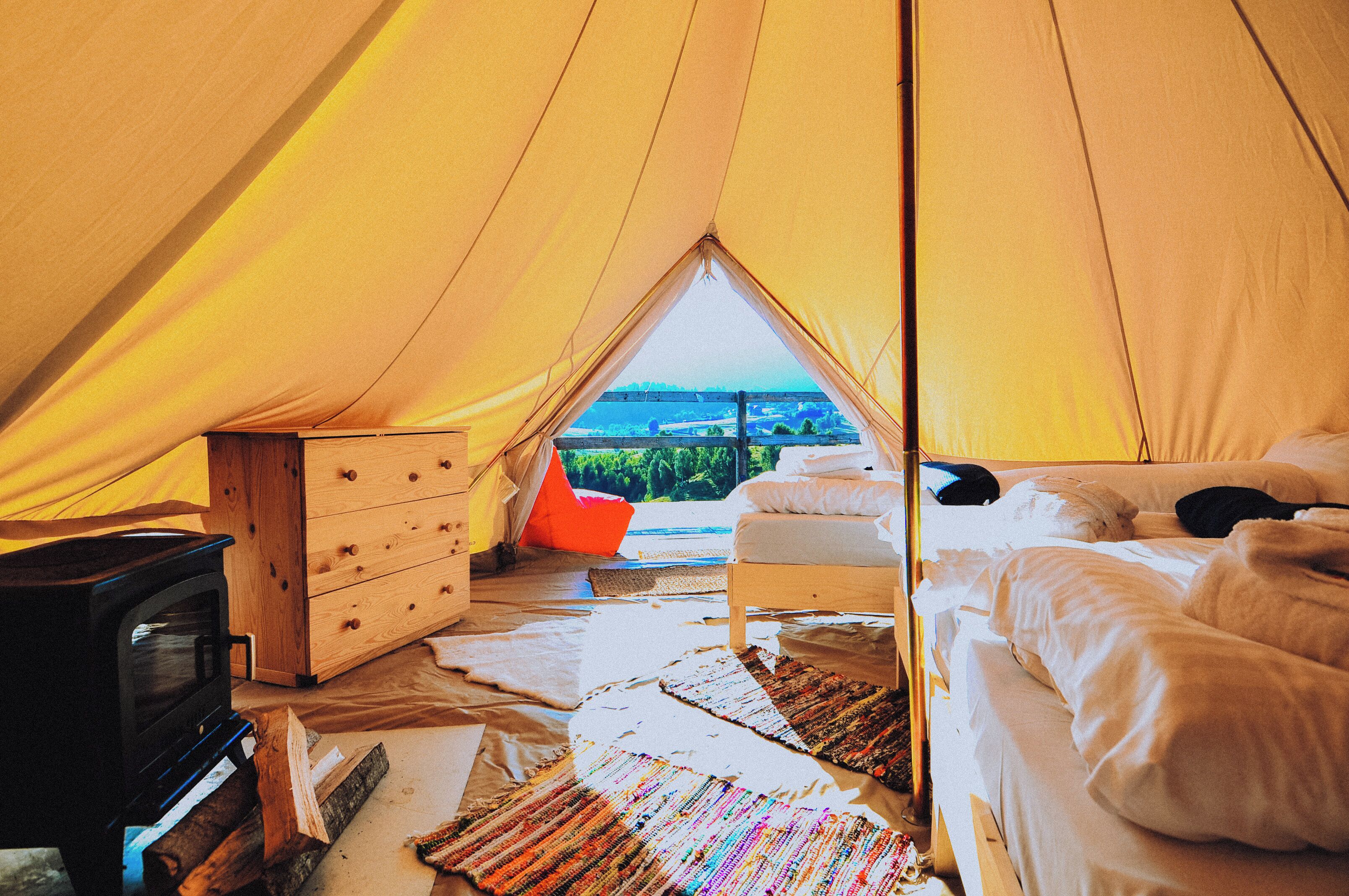 A tent with a bed, a dresser, and a wood stove.