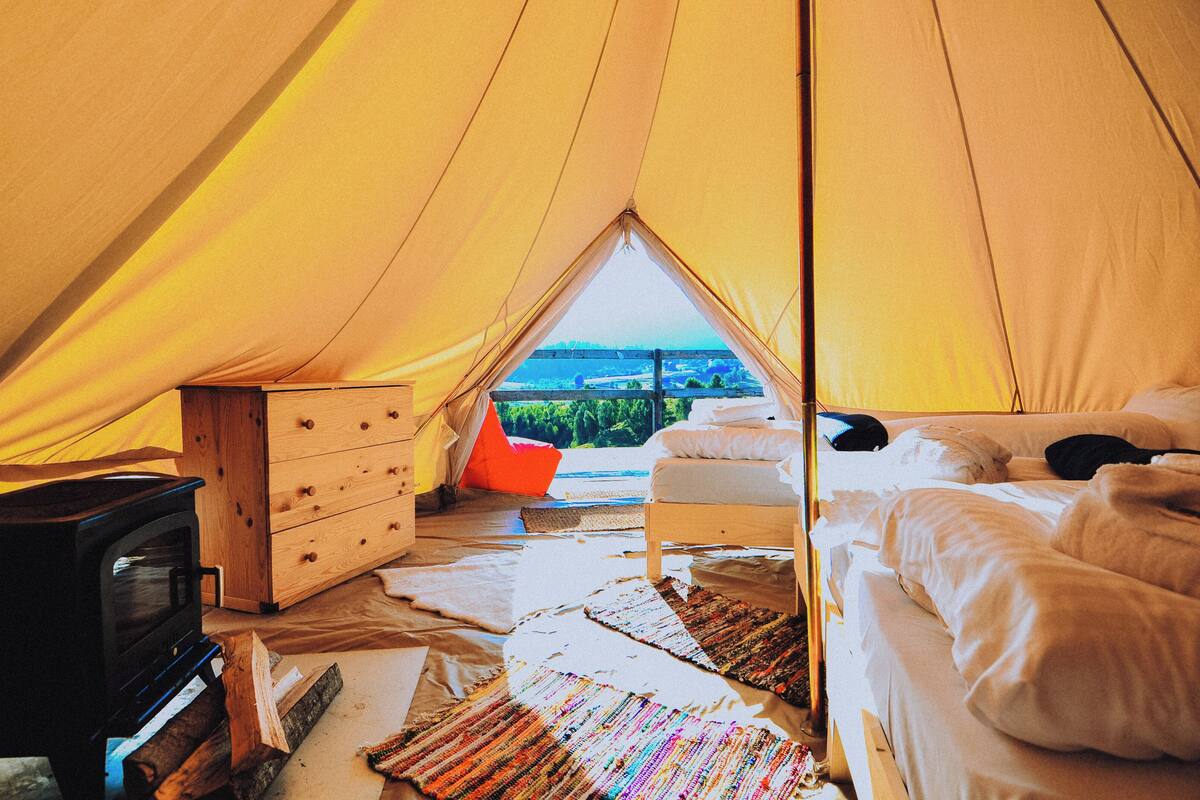 Een tent met een bed, een dressoir en een houtkachel.