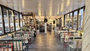 Ein großzügiges Restaurant mit hohen Decken und großen Fenstern, das einen Blick auf die Außenwelt bietet. Tische und Stühle sind reihenweise angeordnet, und es gibt eine zentrale Theke.