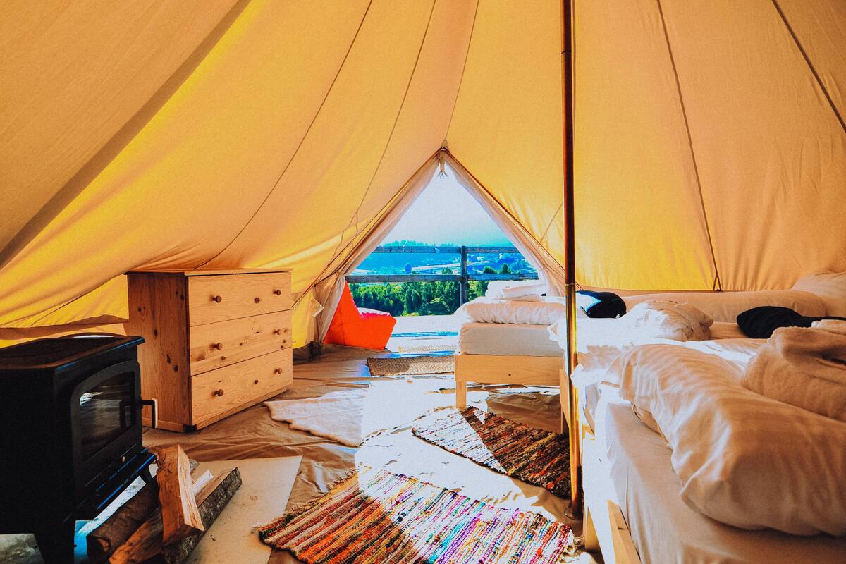 Een tent met een bed, een dressoir en een houtkachel.