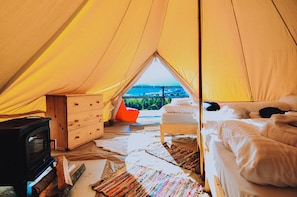 Une tente équipée d’un lit, d’une commode, d’un réchaud et offrant une vue sur le paysage.