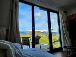 Un dormitorio con un gran ventanal corredera que da a un balcón con vistas a la montaña.