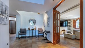 A spacious living area with a high ceiling, a dining table with chairs, a fireplace, and a kitchen visible through an open door. - Large villa with huge garden and swimming pool, perfect for groups and events (Elx)