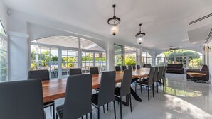 Un comedor amplio con una larga mesa de madera y sillas modernas, ventanas grandes que ofrecen vistas a zonas verdes y elegantes lámparas colgantes.