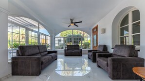 Una habitación amplia con un ventanal grande, ventilador de techo y un área de estar central con sofás.