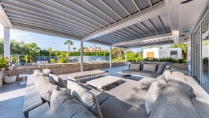 Un espacio de estar al aire libre, cubierto, con mobiliario moderno y vistas del paisaje circundante.