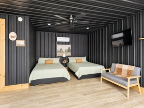 Une chambre avec deux lits, un ventilateur de plafond, une télévision et un banc en bois.