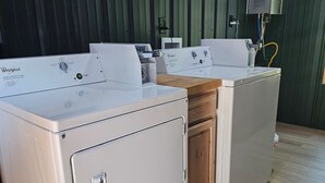 Une buanderie équipée de deux machines à laver Whirlpool, d’un plan de travail en bois et d’un mur peint en vert.