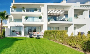 A modern multi-story residential building with balconies, a well-maintained lawn, and outdoor seating. - Elegant 2-Bed Apartment | Alcazaba Lagoon (1604) (Casares)
