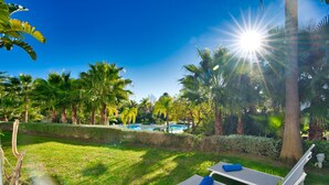 A sunny outdoor area with two lounge chairs, a pool, and palm trees. - Stylish 2-Bed Apartment | Alcazaba Lagoon (303) (Casares)