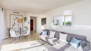 Una sala de estar moderna con un sofá gris, una mesa de centro de vidrio y un comedor con una mesa y sillas blancas.