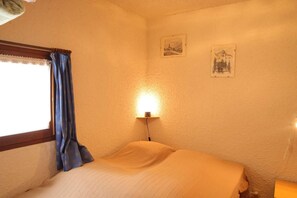 A room with a bed, a window with curtains, a wall-mounted lamp, and two framed pictures. - 250m from ski slopes, 2nd floor, view mountain, balcony, tv, ski locker, 35m², Auris en Oisans (Auris)