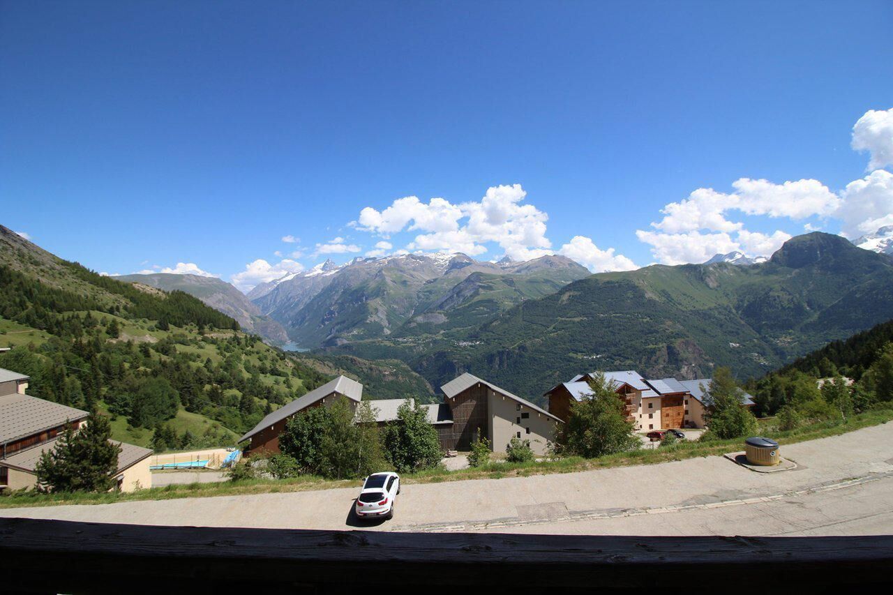 A mountain village with traditional houses, a parking area, and a clear view of the surrounding mountains.
