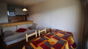 A compact room with a bed, a sofa, a small kitchenette, and a dining table.