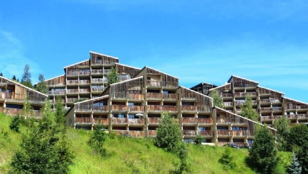 A modern hotel with multiple balconies, set on a hillside with lush greenery.
