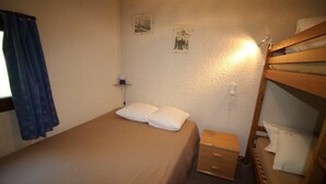 A single bed with two pillows, a bedside table with a lamp, and a bunk bed to the right.