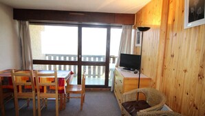 Une pièce au décor intérieur en bois, une table à manger avec des chaises, un téléviseur posé sur un meuble, et un balcon avec vue.