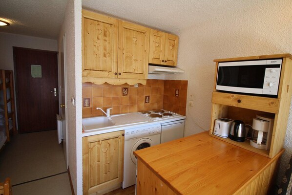 A compact kitchen with wooden cabinets, a microwave, a stove, a washing machine, and a coffee maker.