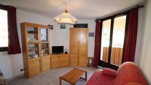 Un salon avec un meuble en bois, un téléviseur, une table en bois et un canapé rouge.
