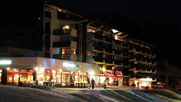 Un hôtel à plusieurs étages doté d’espaces extérieurs aménagés et d’une piste de ski en premier plan.