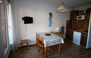 Una cocina pequeña con una mesa de comedor, sillas de madera, un microondas y un refrigerador.
