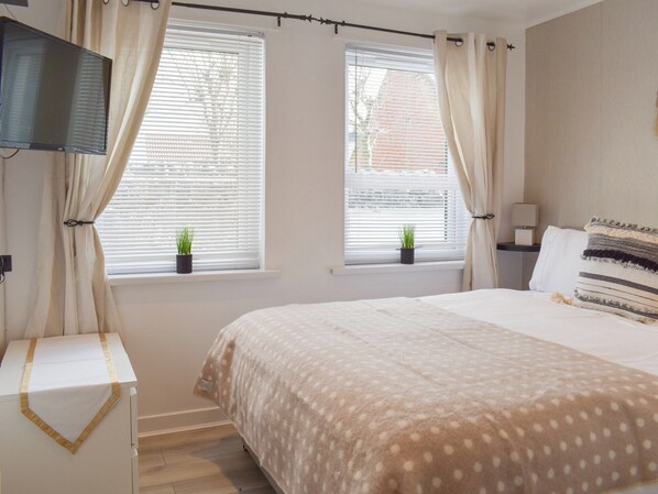 Una camera da letto con un letto, due finestre con tende, una TV, un comodino e una lampada.