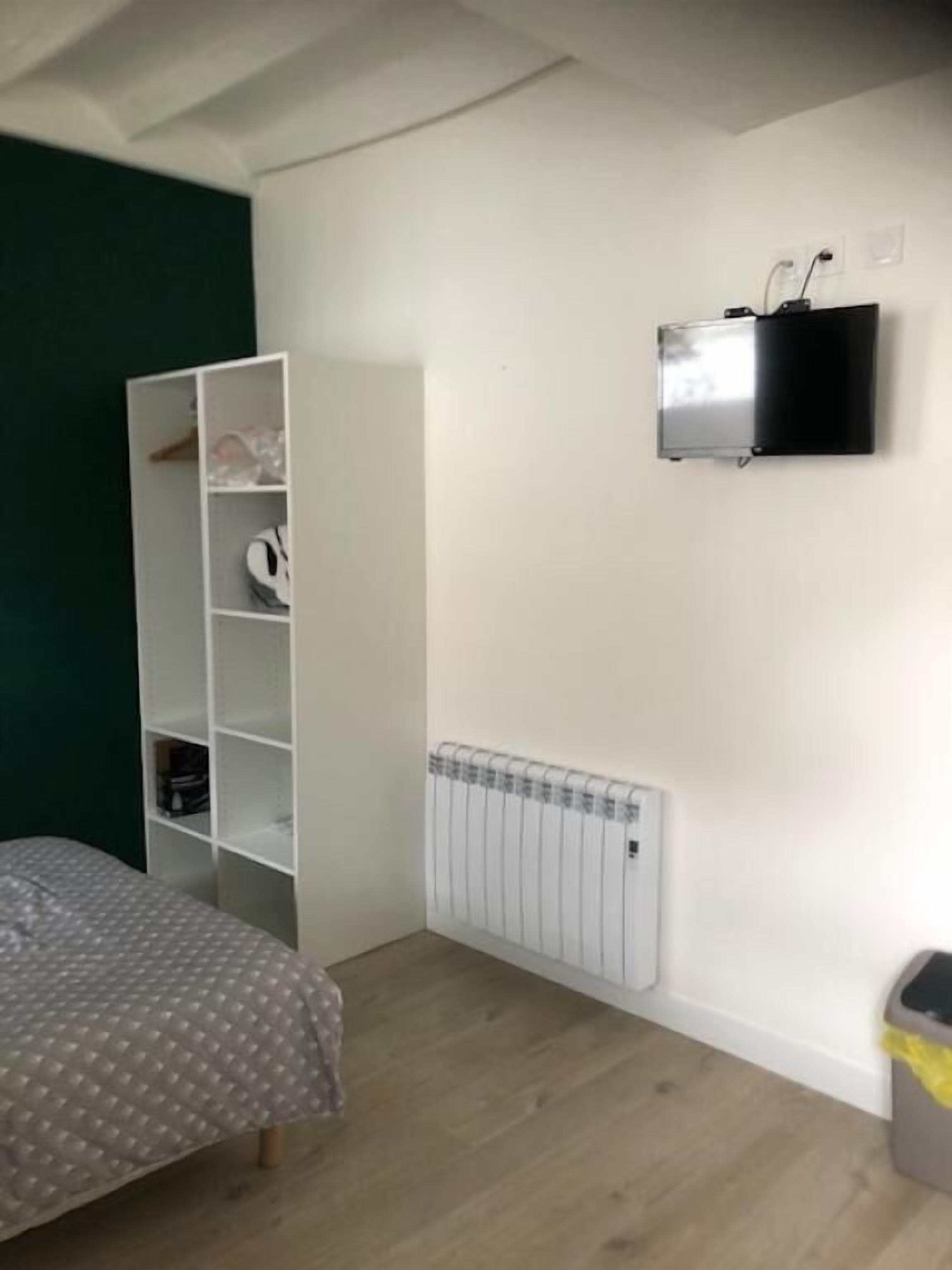 Quarto com cama, guarda-roupa branco, radiador e televisão na parede.