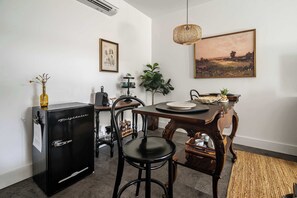 Una cucina compatta con frigorifero, un tavolo da pranzo con sedie, una lampada a sospensione e un quadro raffigurante un paesaggio appeso al muro.
