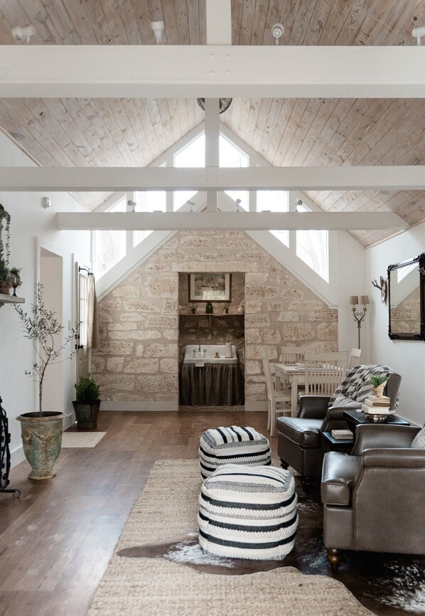 Un loft amplio con techo alto, vigas de madera a la vista, chimenea de piedra y un rincón de descanso acogedor con otomanas y un sofá de cuero.