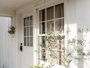 A white door with a window, a wreath, and a plant in front.