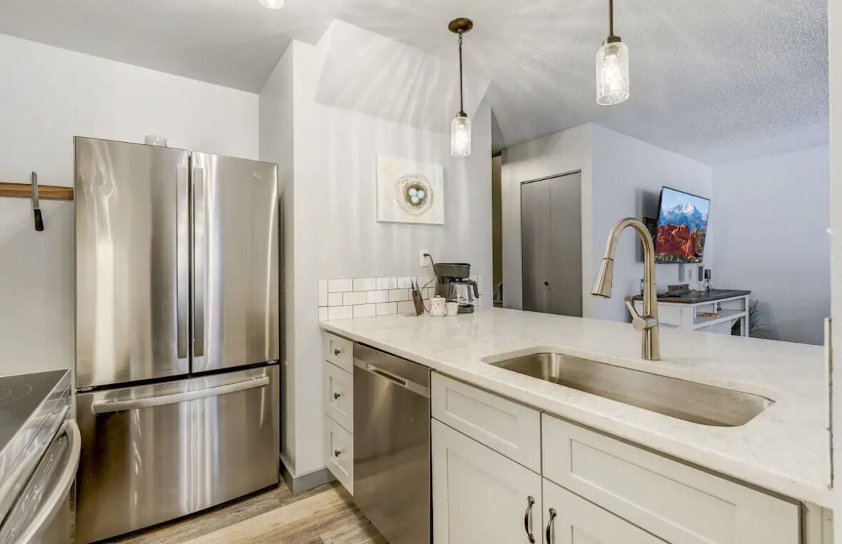 A modern kitchen with stainless steel appliances, a white countertop, and a large sink.