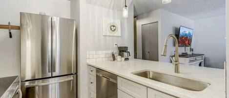 A modern kitchen with stainless steel appliances, a white countertop, and a large sink.