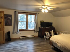 A bedroom with a bed, a ceiling fan, a window with curtains, a dresser, and a television.