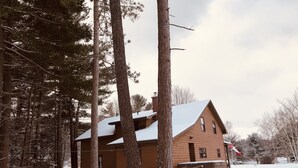 A wooden cabin with a snow-covered roof, surrounded by tall pine trees.