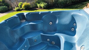 A hot tub with multiple jets, surrounded by a wooden fence and greenery.