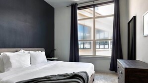 A hotel room with a bed, a dresser, a nightstand, and a window with curtains.