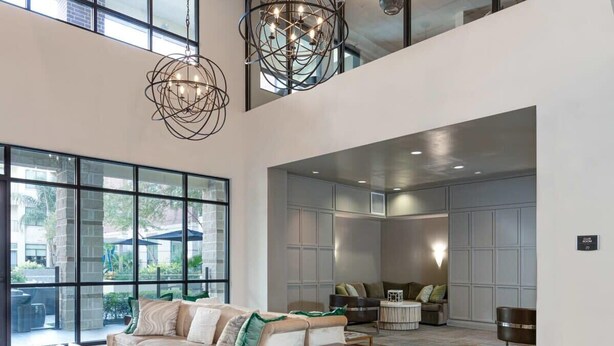 A spacious living area with a high ceiling, large windows, and modern lighting fixtures.