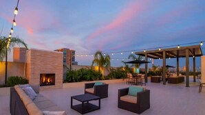 A rooftop patio with outdoor seating, a fireplace, string lights, and a view of the city skyline.