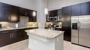 A modern kitchen with dark cabinets, stainless steel appliances, and a granite island.